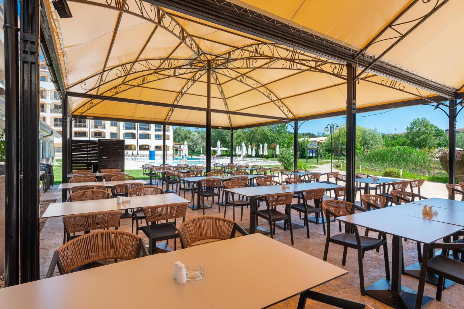 Sunrise All Suites Resort āra terase zem nojumes ar pītiem krēsliem un skatu uz viesnīcas dārzu un baseinu