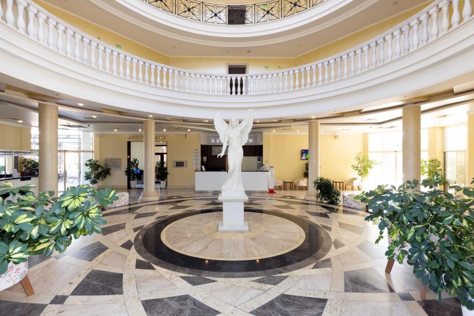 Rome Palace Deluxe viesnīcas plašais vestibils ar marmora grīdu, centrālo statuju un balkonu galeriju Saulainajā Krastā, Bulgārijā