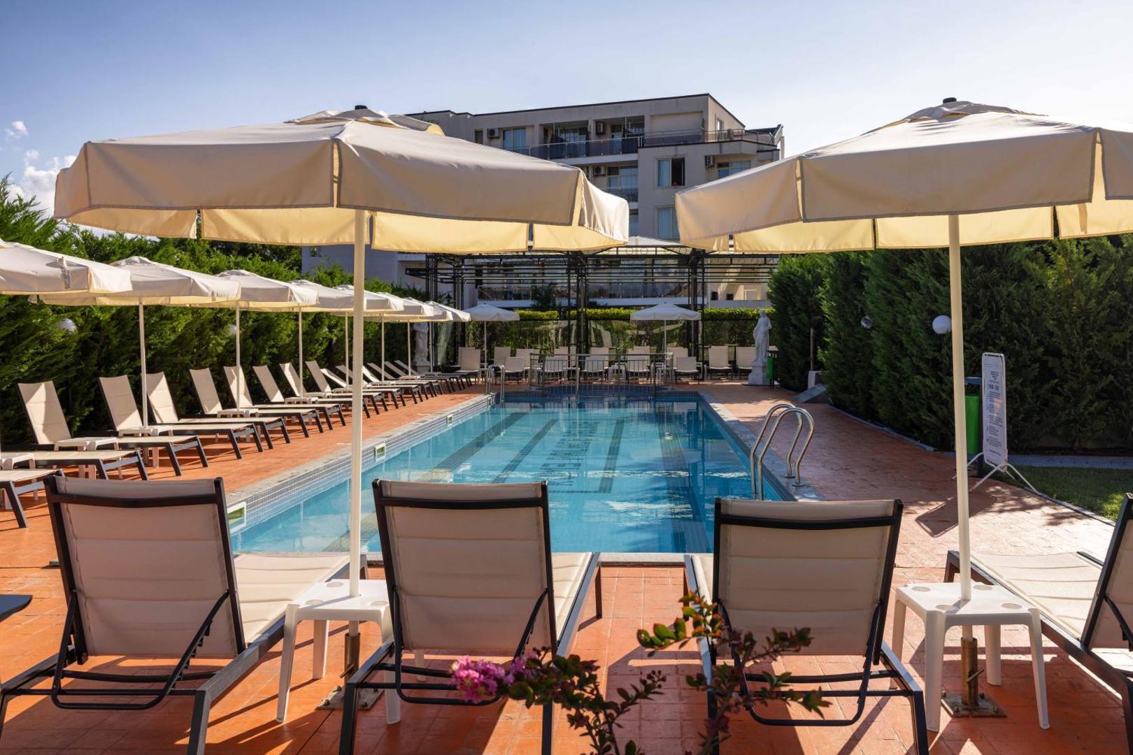 Rome Palace Deluxe āra baseins ar saulessargiem un sauļošanās krēsliem, ko ieskauj zaļumi un viesnīcas korpuss