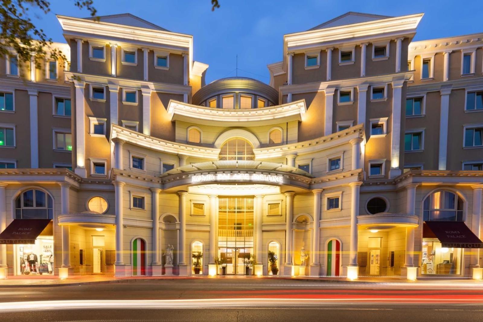 Rome Palace Deluxe viesnīcas galvenā ieeja vakarā Saulainajā krastā, Bulgārijā — izgaismota klasiskā arhitektūra ar kolonnām un boutique veikaliem