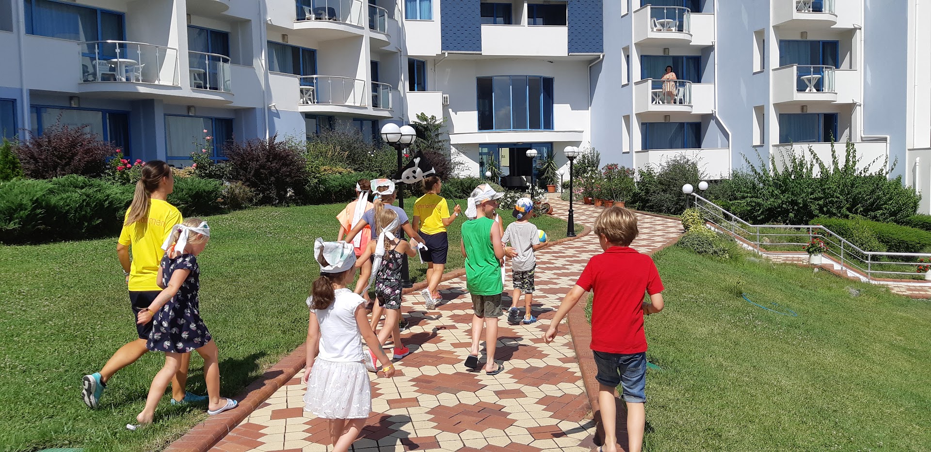 Bērnu animācijas aktivitātes Sineva Beach viesnīcas teritorijā, kur animatori vada grupu pa bruģētu taciņu