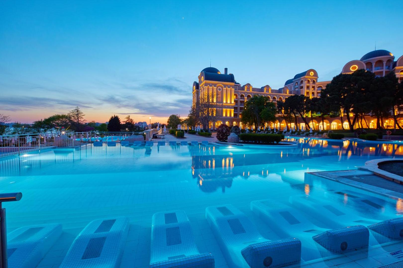 Alua Sunny Beach Resort & Spa izgaismotais baseins un viesnīcas fasāde vakarā ar ērtiem ūdens zviļņiem relaksācijai zem klajas debess