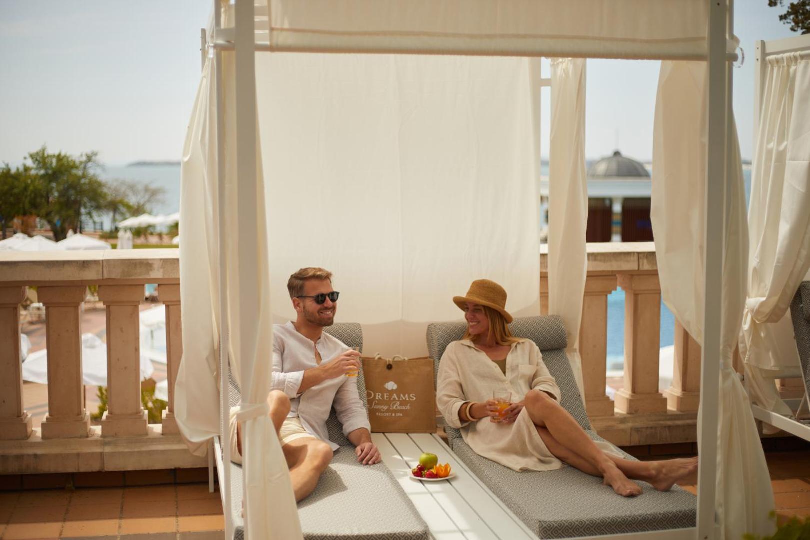 Atpūtas zona ar baldahīniem Alua Sunny Beach Resort & Spa terasē, kur pāris bauda dzērienus un augļus