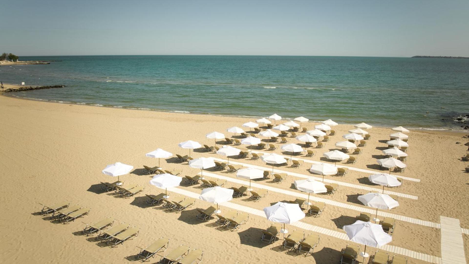 Alua Sunny Beach Resort & Spa plašā smilšu pludmale ar daudziem baltiem saulessargiem un sauļošanās krēsliem Saulainajā krastā
