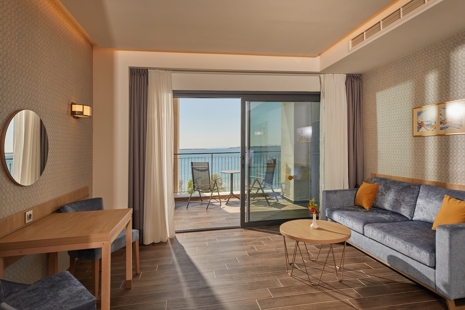 Alua Sunny Beach Resort & Spa viesistabas zona ar pelēku dīvānu un skatu caur stikla durvīm uz jūru