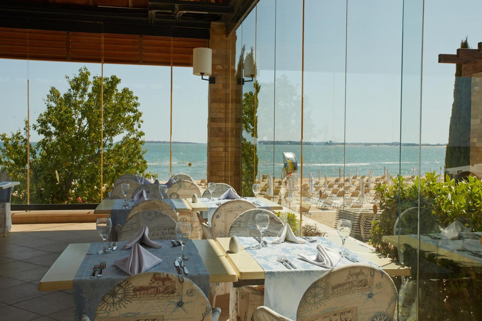Alua Sunny Beach Resort & Spa restorāns ar stiklotām sienām un skatu uz privāto pludmali un saulessargiem.