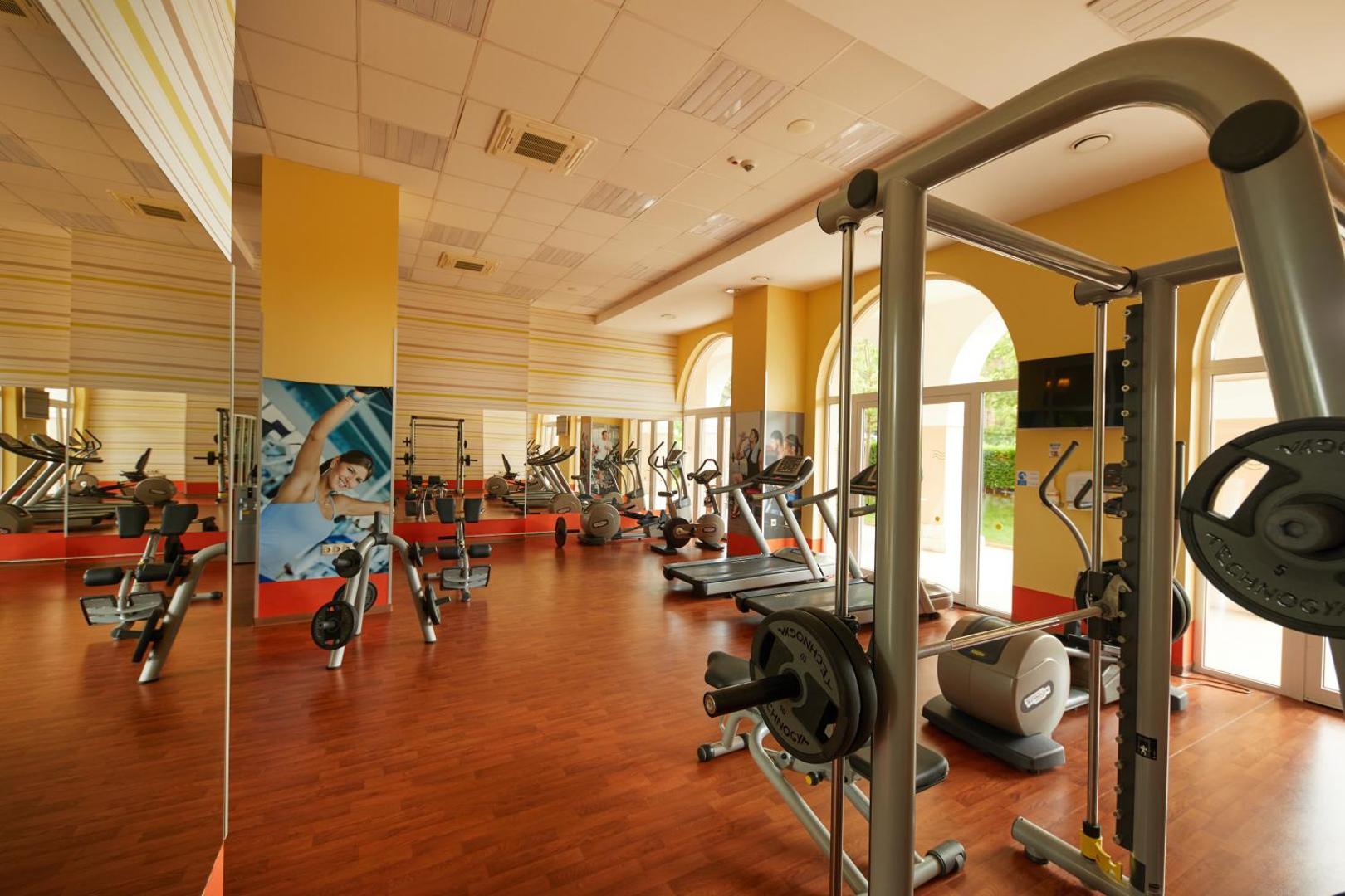 Alua Sunny Beach Resort & Spa gaišs fitness centrs ar Technogym skrejceļiem, trenažieriem un lieliem logiem uz dārzu Bulgārijā.