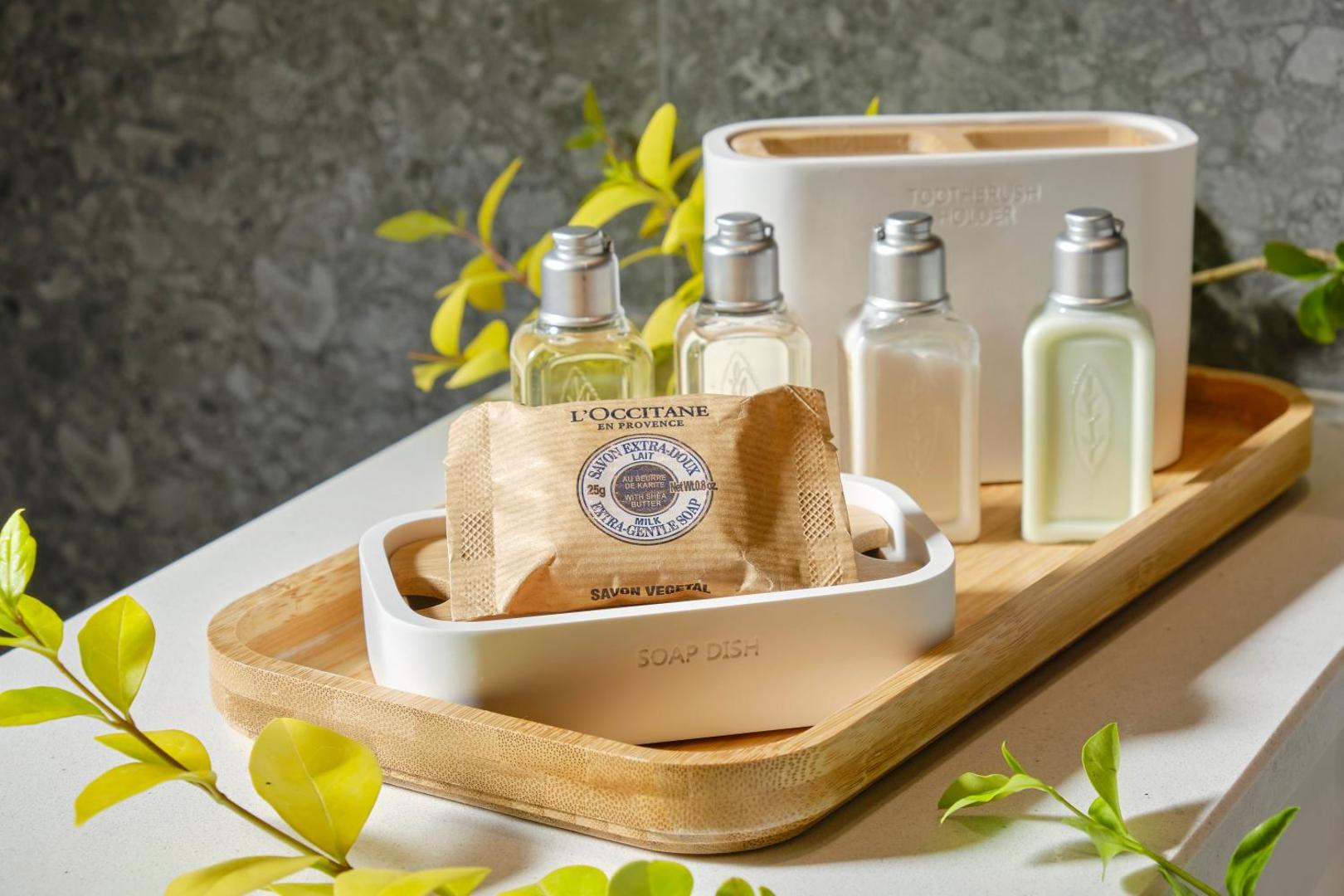 L'Occitane kosmētikas piederumi Viva Mare Beach Hotel numurā — ziepes un šampūni uz koka paliktņa vannas istabā