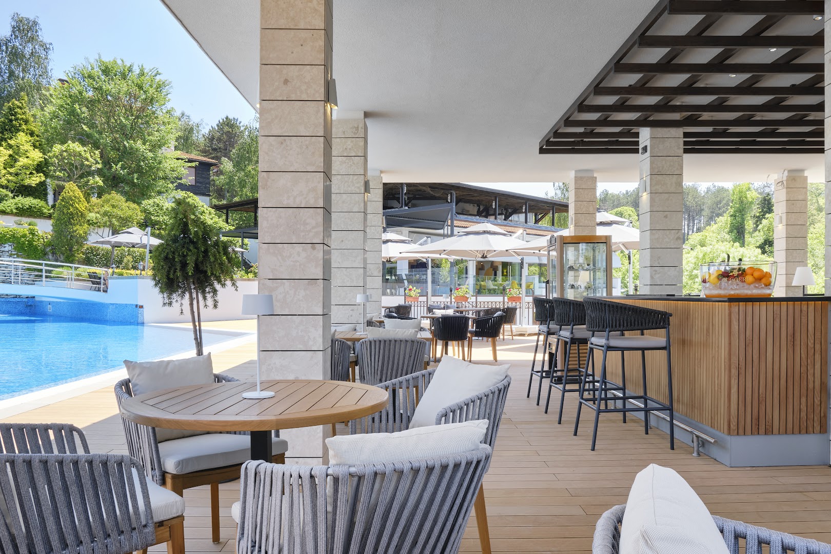 Viva Mare Beach Hotel āra bārs un terase pie baseina ar modernām mēbelēm, saulessargiem un skatu uz zaļo apkārtni