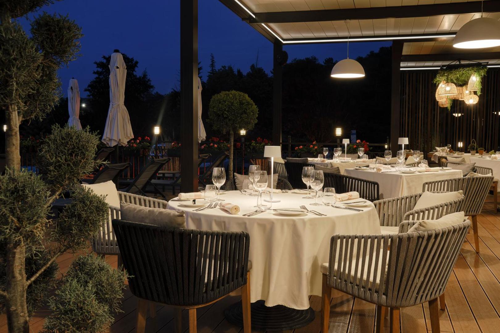 Viva Mare Beach Hotel restorāna āra terase vakarā ar klātiem galdiem, elegantiem krēsliem un siltu apgaismojumu zem nojumes