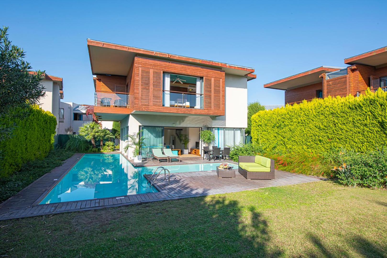 Lykia World Antalya moderna divstāvu villa ar privātu baseinu, koka terasi un iekoptu zālienu, ko norobežo augsts dzīvžogs