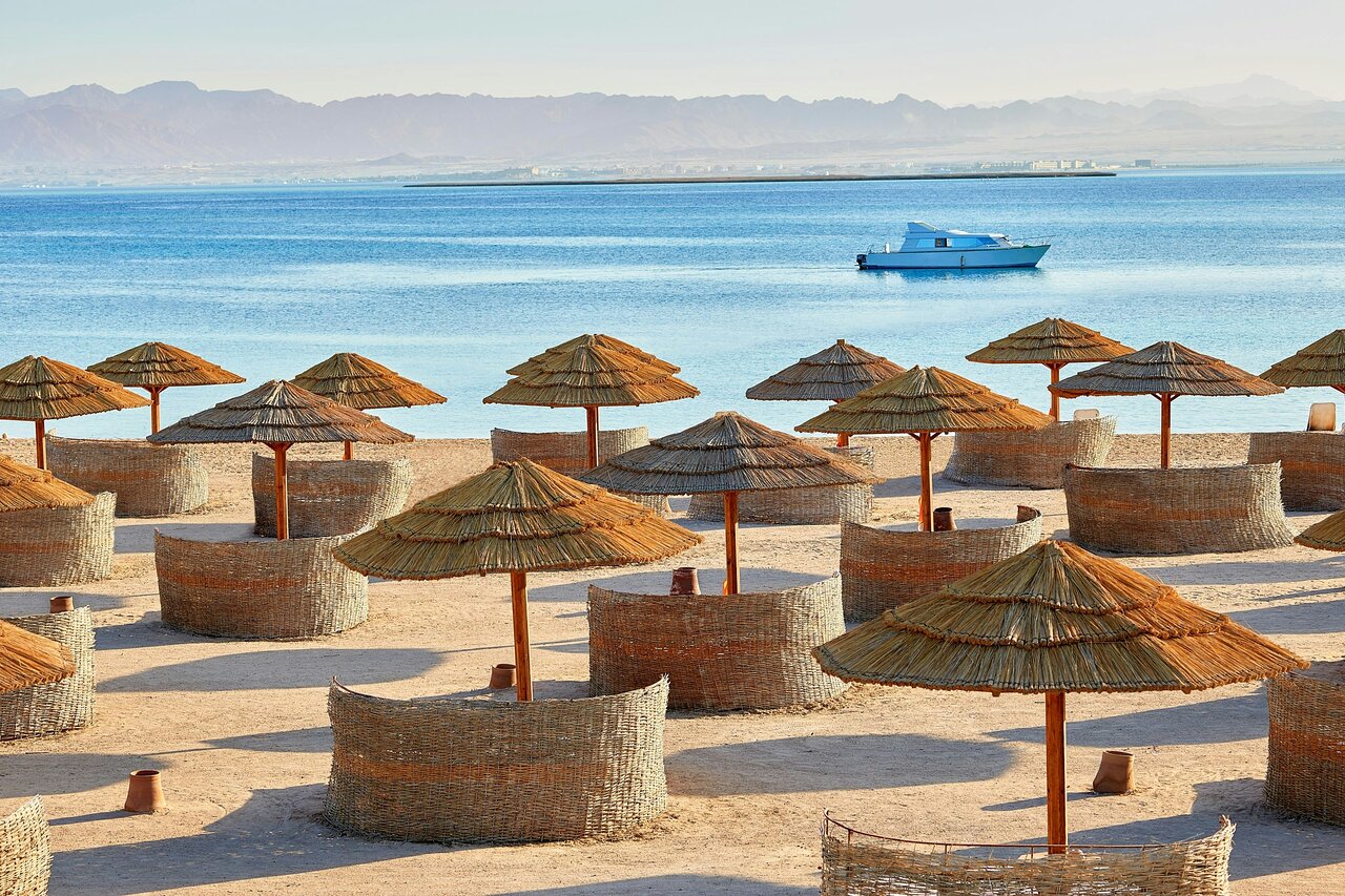 Sheraton Soma Bay Resort pludmales zona ar salmu saulessargiem, vēja aizsegiem un jahtu Sarkanajā jūrā
