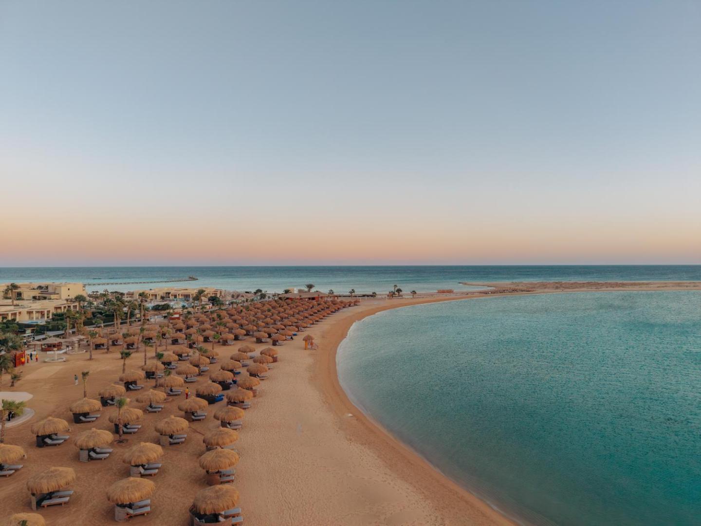 Sheraton Soma Bay Resort plašā smilšu pludmale ar saulessargiem un skatu uz Sarkano jūru saulrieta laikā Somabejā