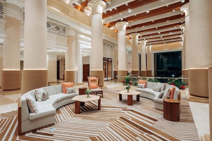 Sheraton Soma Bay Resort plašā atpūtas zona ar pusapaļiem dīvāniem un skatu uz vakara ainavu caur lielajiem logiem