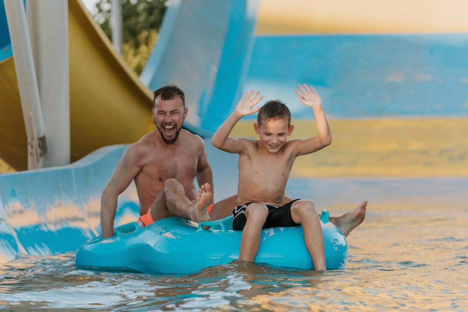 Tēvs un dēls bauda braucienu pa ūdens slidkalniņu ar piepūšamo riņķi Sheraton Soma Bay Resort akvaparkā Sarkanās jūras piekrastē