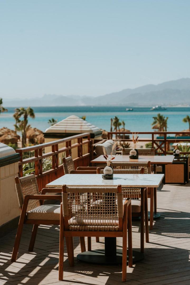 Sheraton Soma Bay Resort āra terase ar galdiņiem un skatu uz Sarkano jūru un kalniem — eleganta vieta brokastīm vai vakariņām