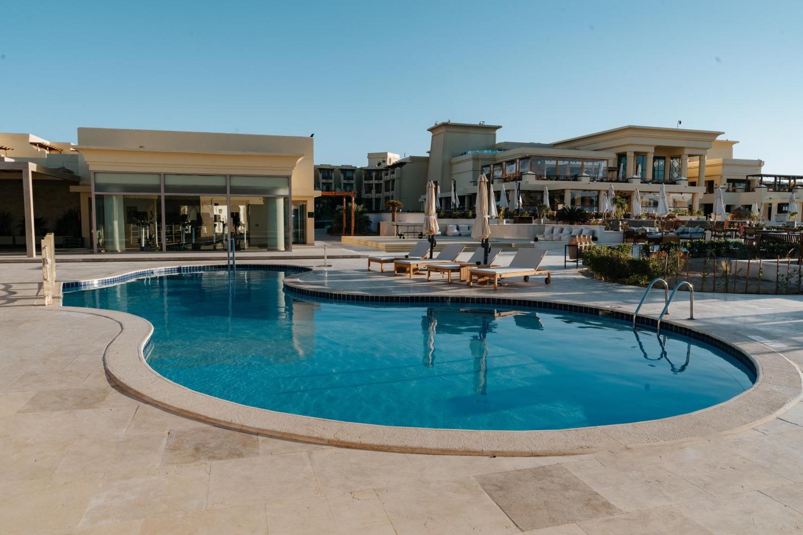 Sheraton Soma Bay Resort āra baseins pie galvenās ēkas ar sauļošanās krēsliem un skatu uz viesnīcas arhitektūru