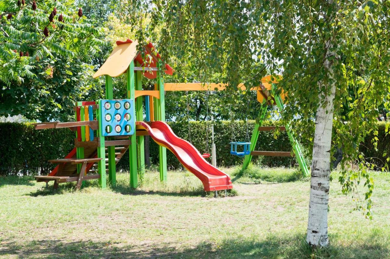 Sineva Park bērnu rotaļu laukums zaļā dārzā ar slidkalniņu un šūpolēm — droša izklaides zona mazākajiem viesiem koku pavēnī