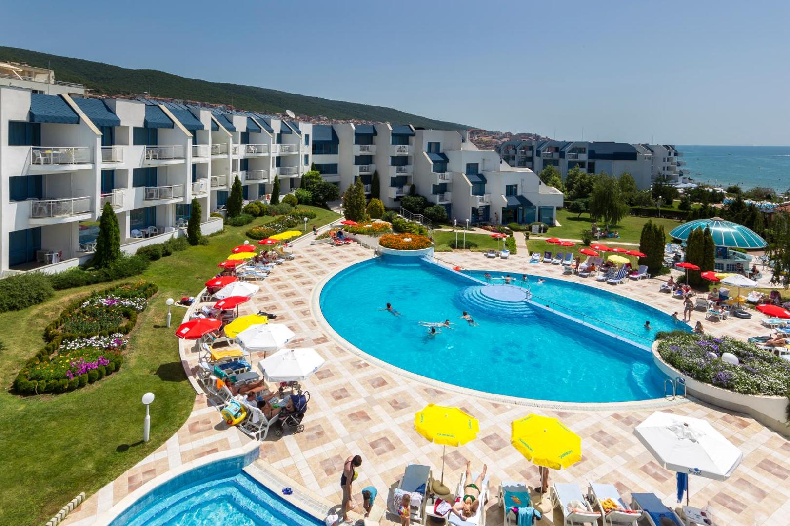Sineva Park viesnīcas teritorija ar lielu āra baseinu, saulessargiem un ēku kompleksu Saulainajā krastā — skats no augšas