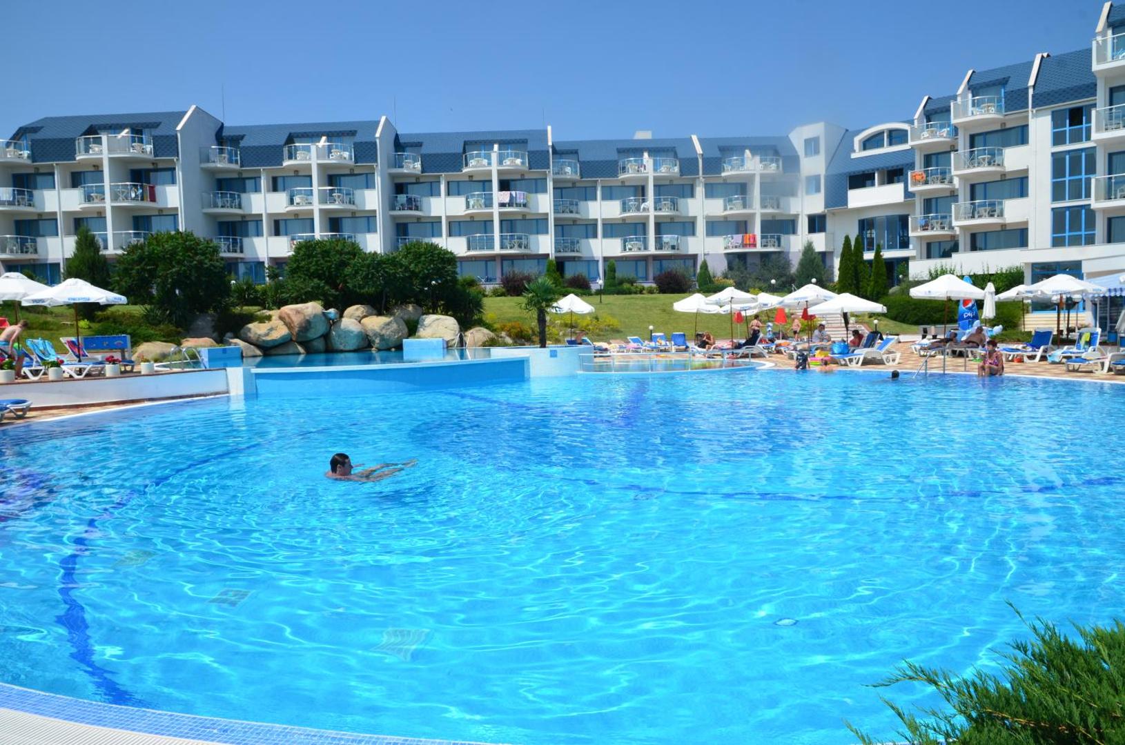 Viesnīcas Sineva Beach galvenais baseins un ēkas fasāde ar balkoniem, apkārtnē labiekārtota sauļošanās zona un apstādījumi