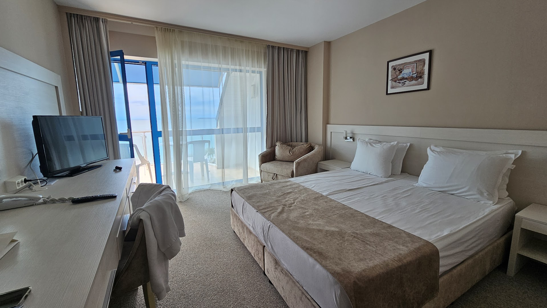 Sineva Beach viesnīcas divvietīgs numurs ar lielu gultu, atpūtas krēslu un izeju uz balkonu ar skatu uz piekrasti