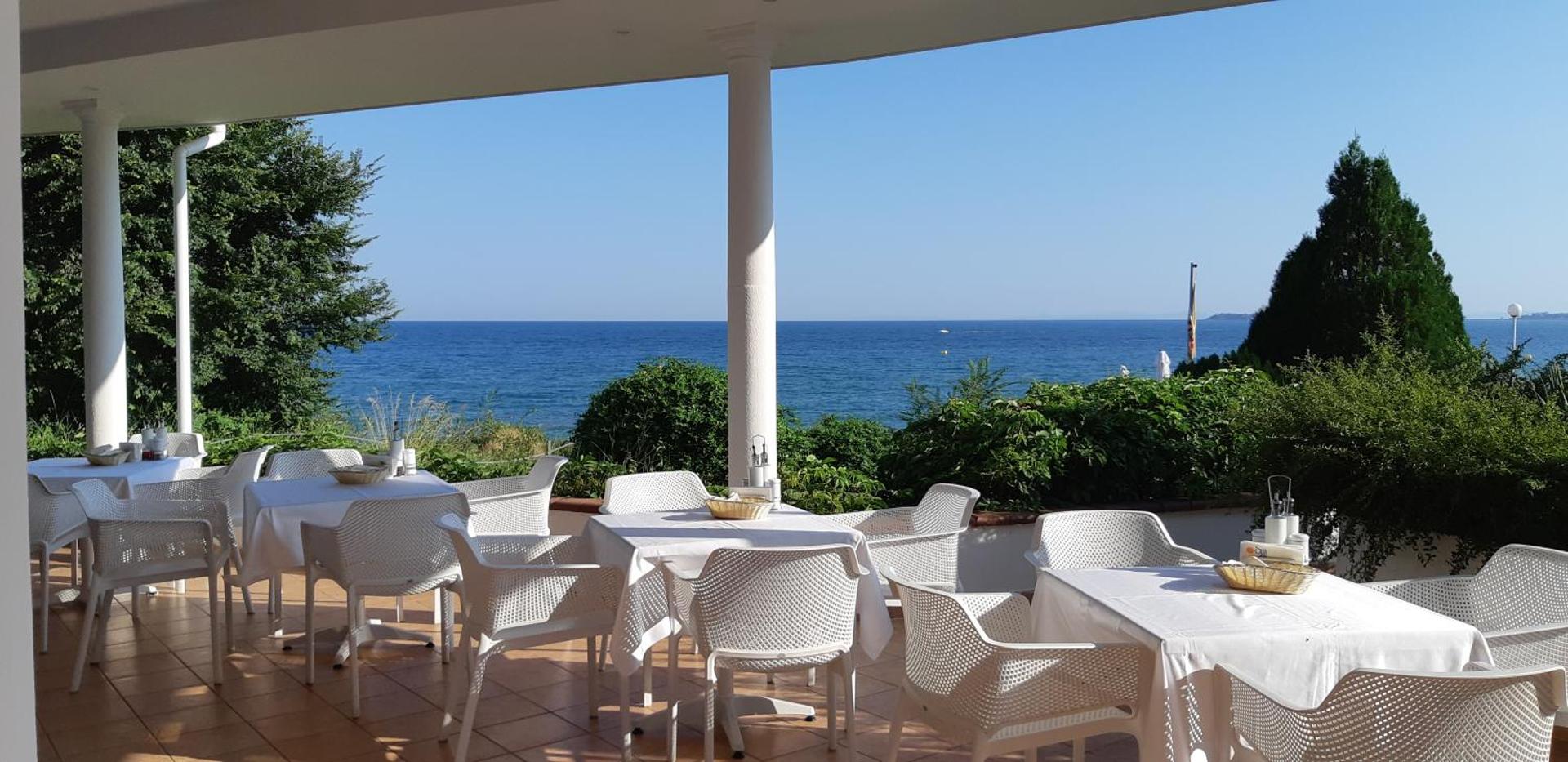 Sineva Beach restorāna terase ar baltiem galdiem un krēsliem, no kuras paveras tiešs skats uz Melno jūru.