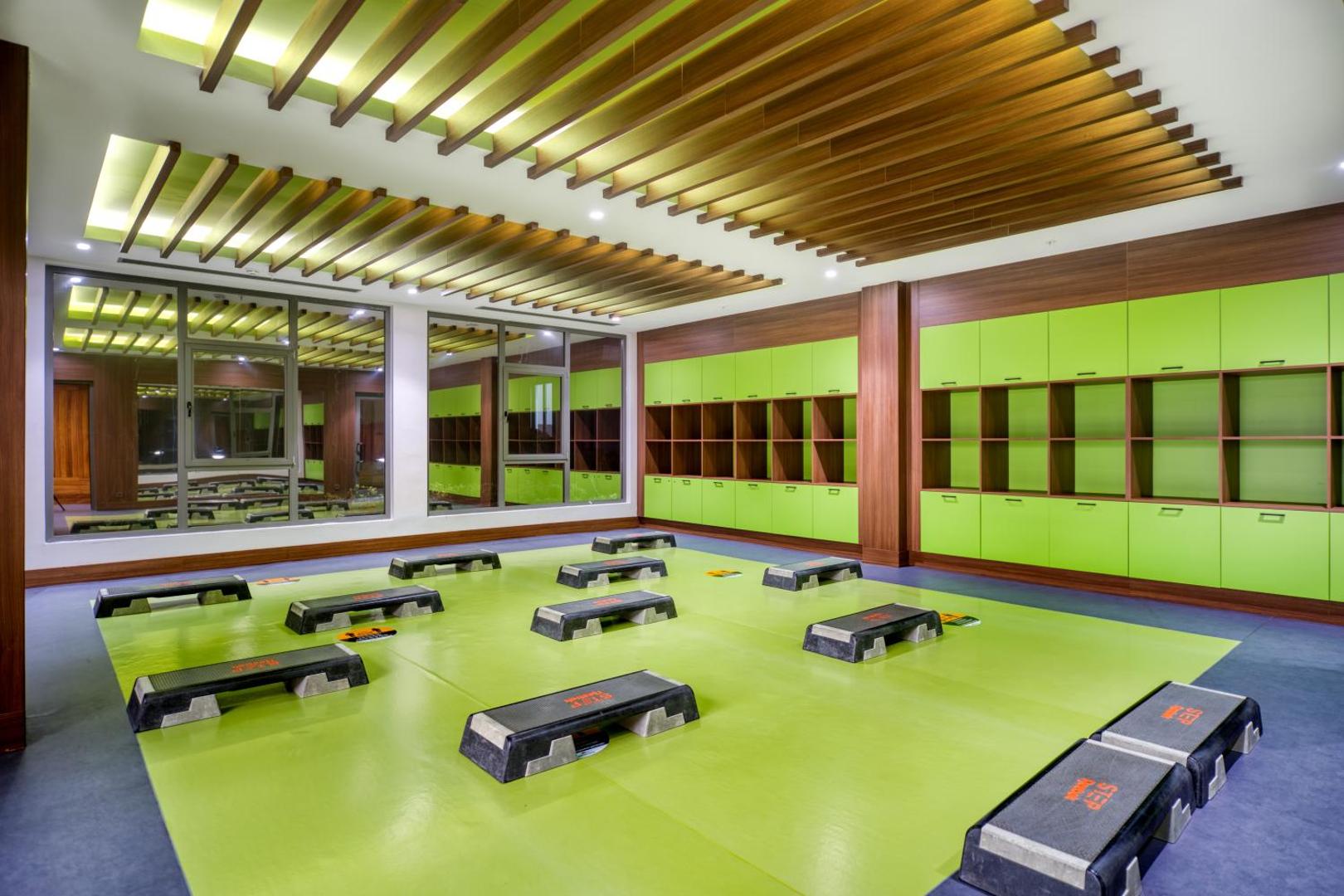 Megasaray Club Belek fitnesa zāle ar stepa platformām un spoguļiem — gaiša telpa sporta nodarbībām un aktīvai atpūtai Antalijas reģionā