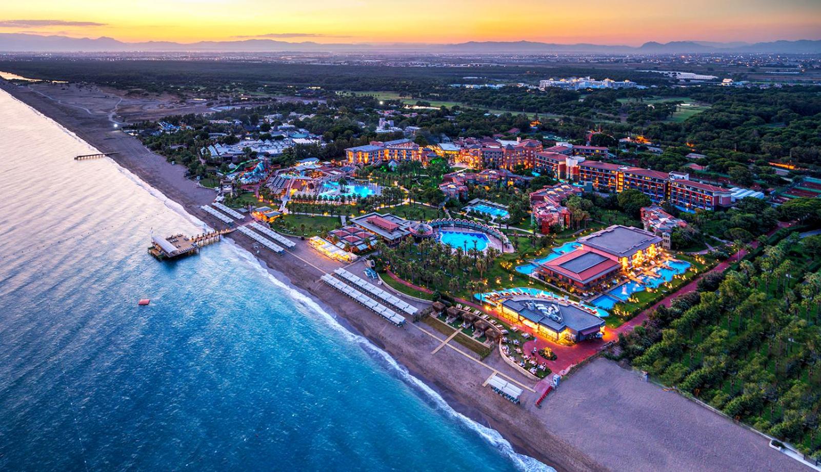 Megasaray Club Belek panorāmas skats no putna lidojuma saulrietā — plaša teritorija pie Vidusjūras ar baseiniem, dārziem un privātu pludmali