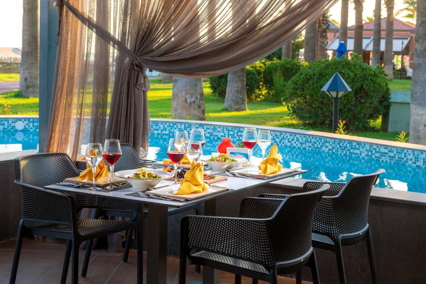 Tuvplāns klātam galdam Megasaray Club Belek restorānā ar vīna glāzēm un uzkodām pie baseina malas