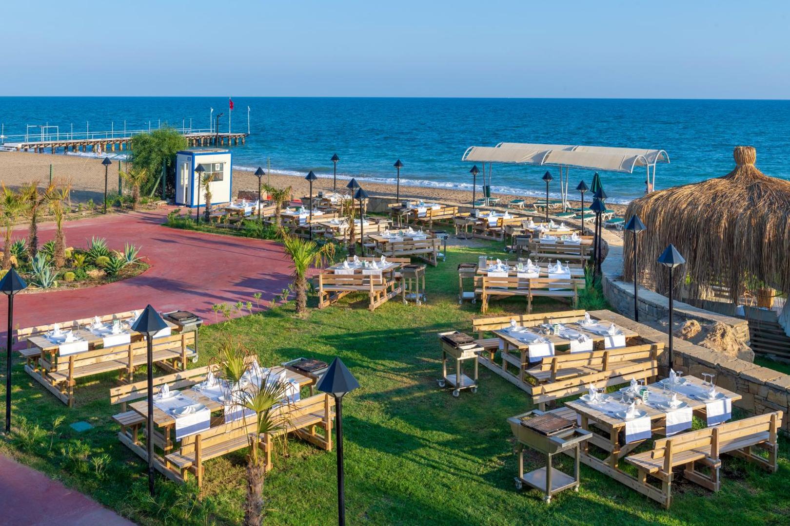 Megasaray Club Belek āra restorāns pie jūras ar koka galdiem zālienā, skatu uz Vidusjūru un privāto piestātni fonā