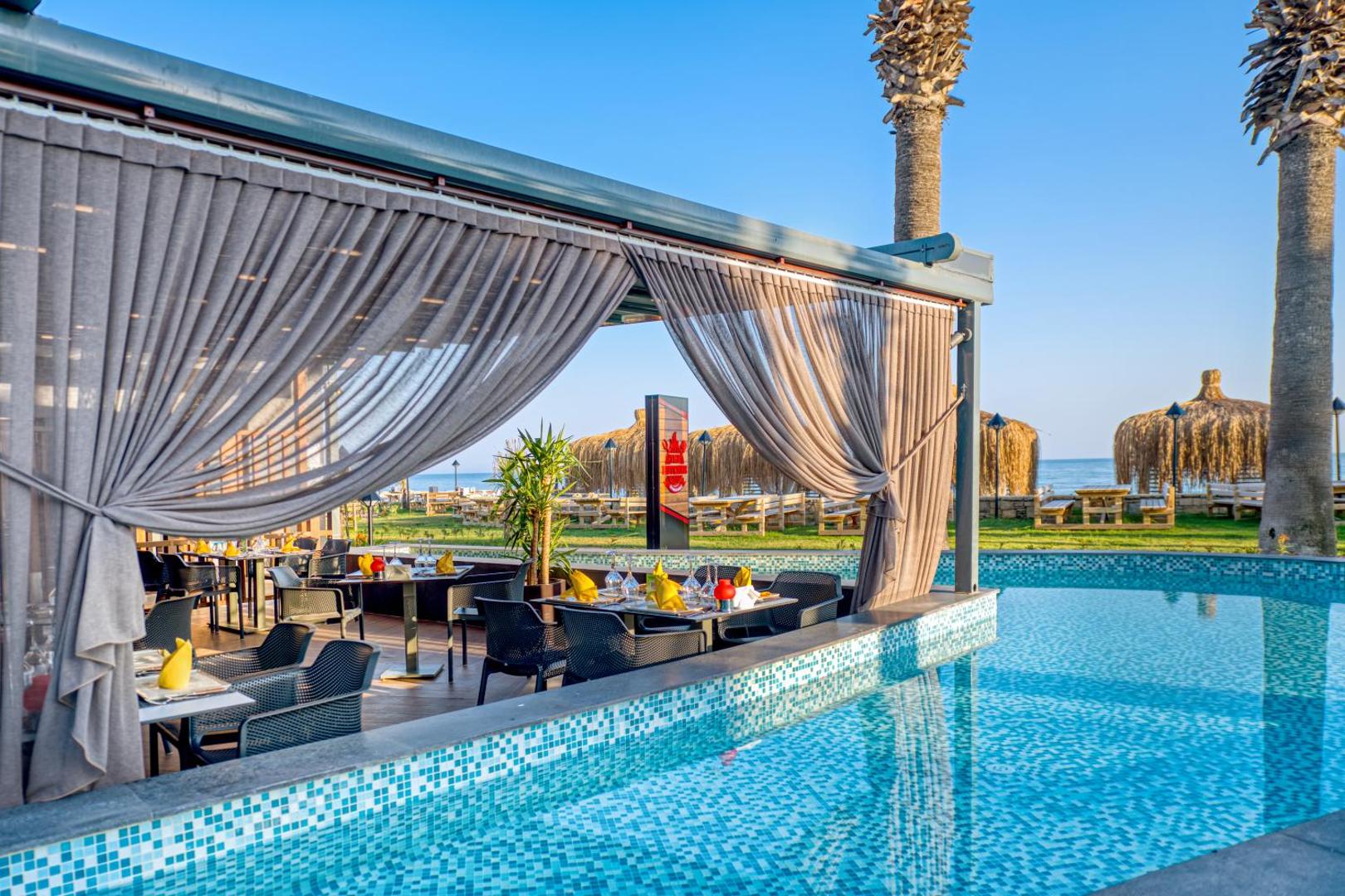 Megasaray Club Belek ēdienkartes restorāna terase pie baseina ar eleganti klātiem galdiem un skatu uz dārzu saulrietā