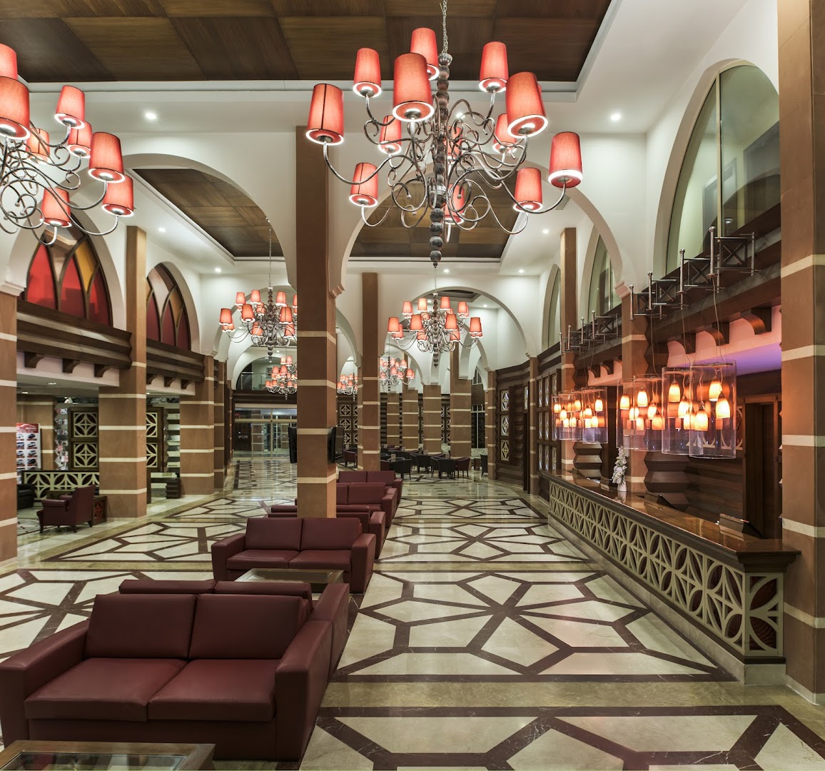 Megasaray Club Belek viesnīcas lobby halle ar greznām lustrām, sarkaniem dīvāniem un rakstainu marmora grīdu elegantā stilā