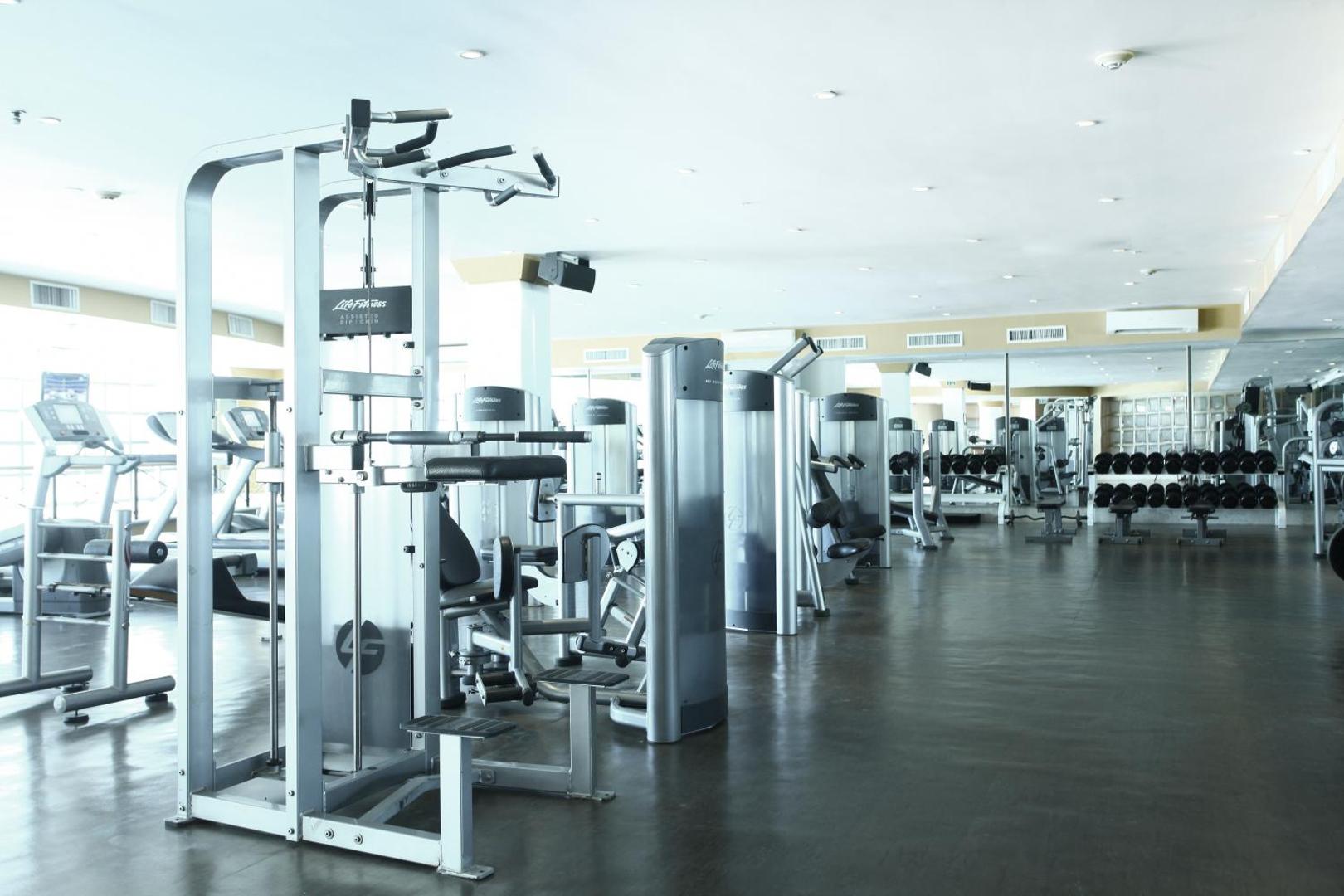 Sandos Cancun plašā trenažieru zāle ar Life Fitness aprīkojumu, spēka trenažieriem un brīvajiem svariem gaišā, modernā interjerā Kankunā.