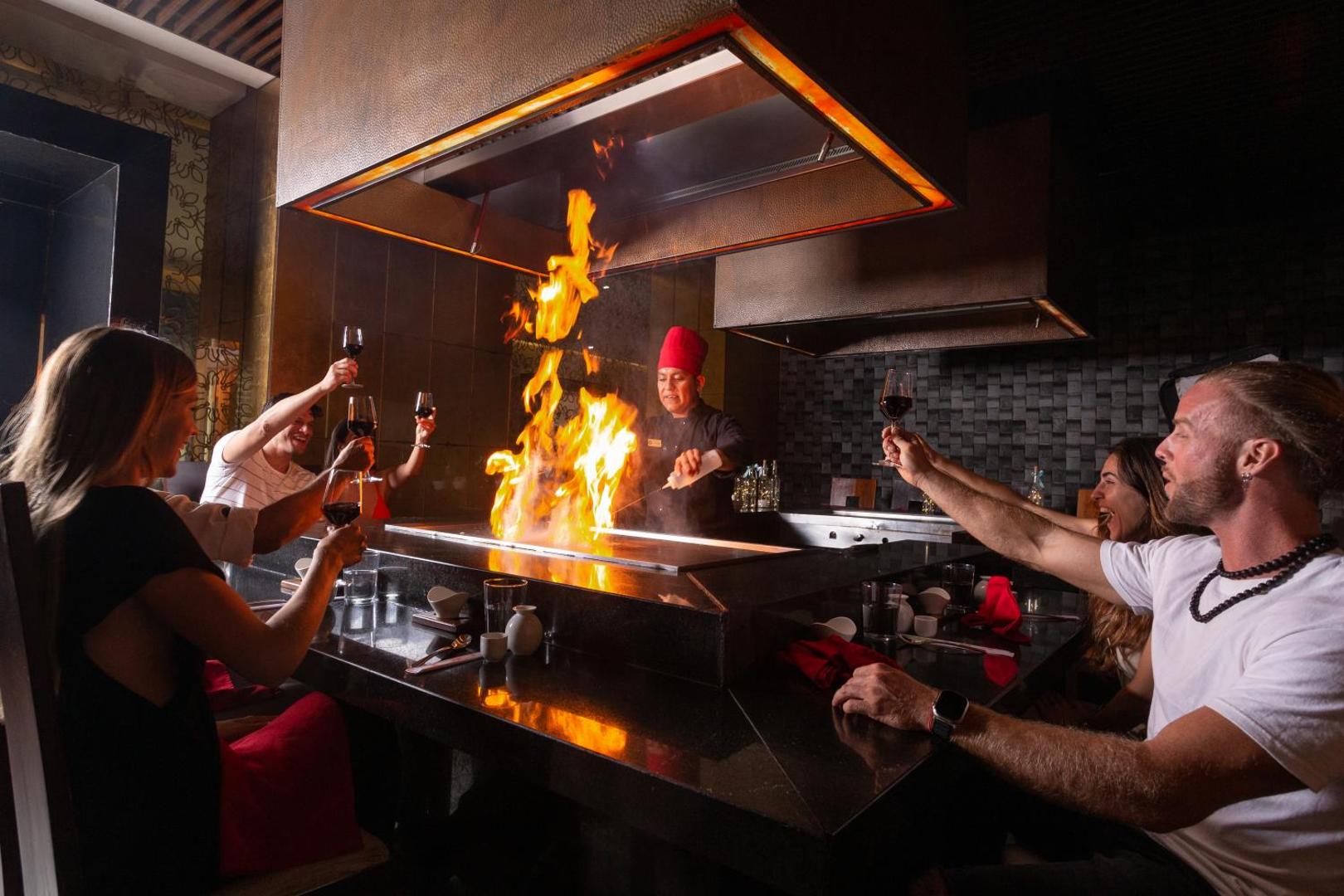 Sandos Cancun viesnīcas teppanyaki restorāns — pavārs demonstrē uguns šovu viesiem, kuri bauda vakariņas pie kopīga galda