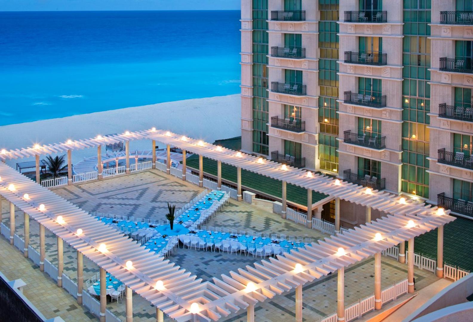 Sandos Cancun āra terase ar svētku galdiem zem pergolas konstrukcijas vakarā pie viesnīcas korpusa un jūras