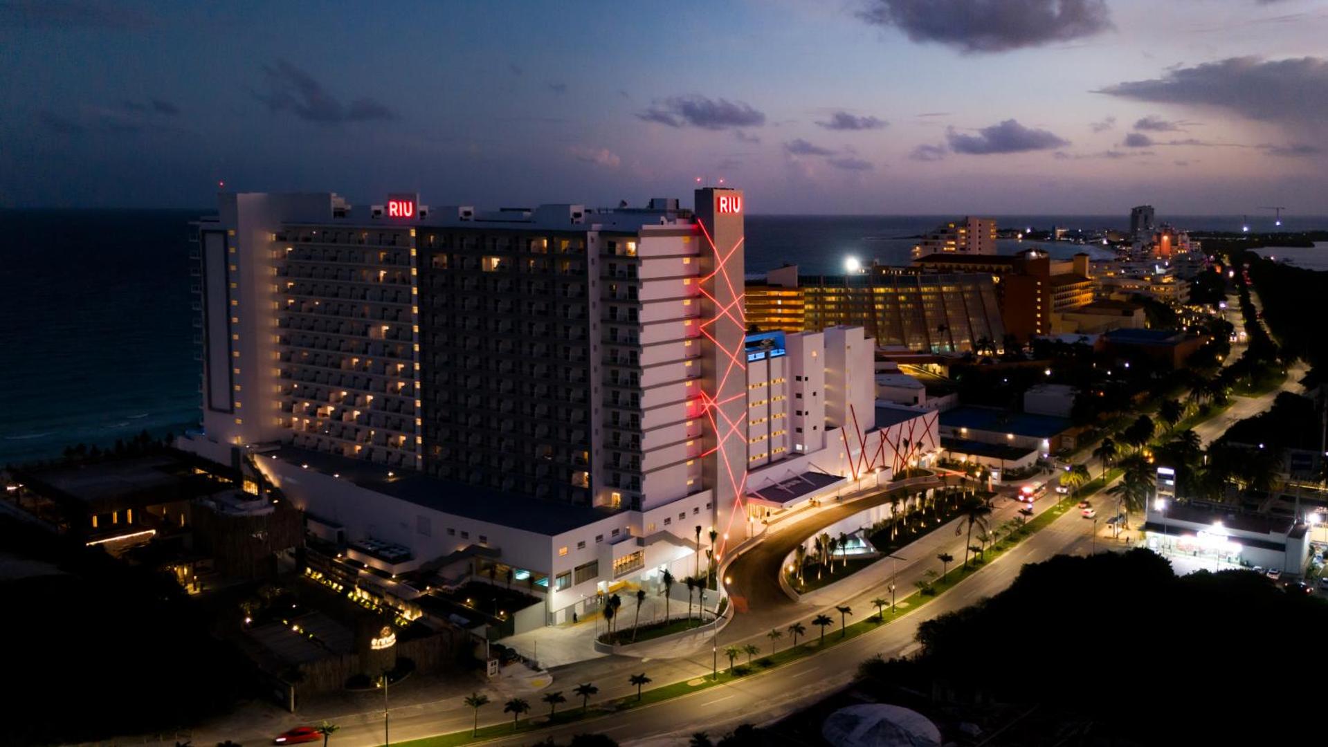 RIU Ventura viesnīcas ēka nakts apgaismojumā Kankunā — izgaismota fasāde ar sarkanām neona līnijām un pilsētas panorāmu fonā