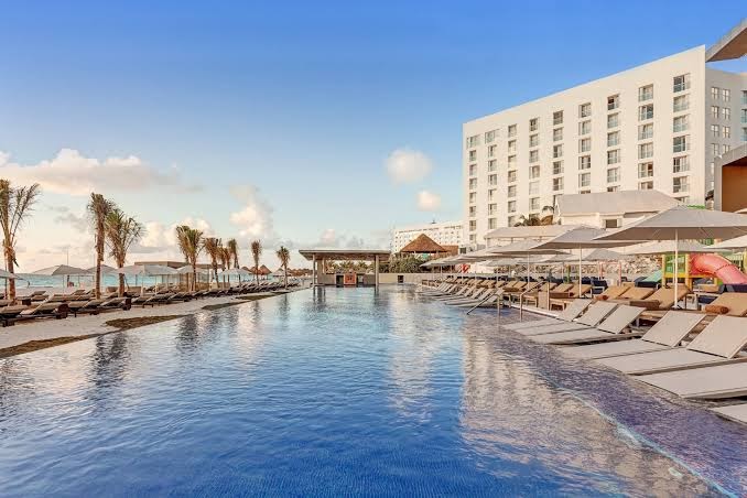 Royalton CHIC Cancun āra baseins ar pārplūdes malu Kankunā, Meksikā — sauļošanās krēsli, saulessargi un skats uz viesnīcas ēku