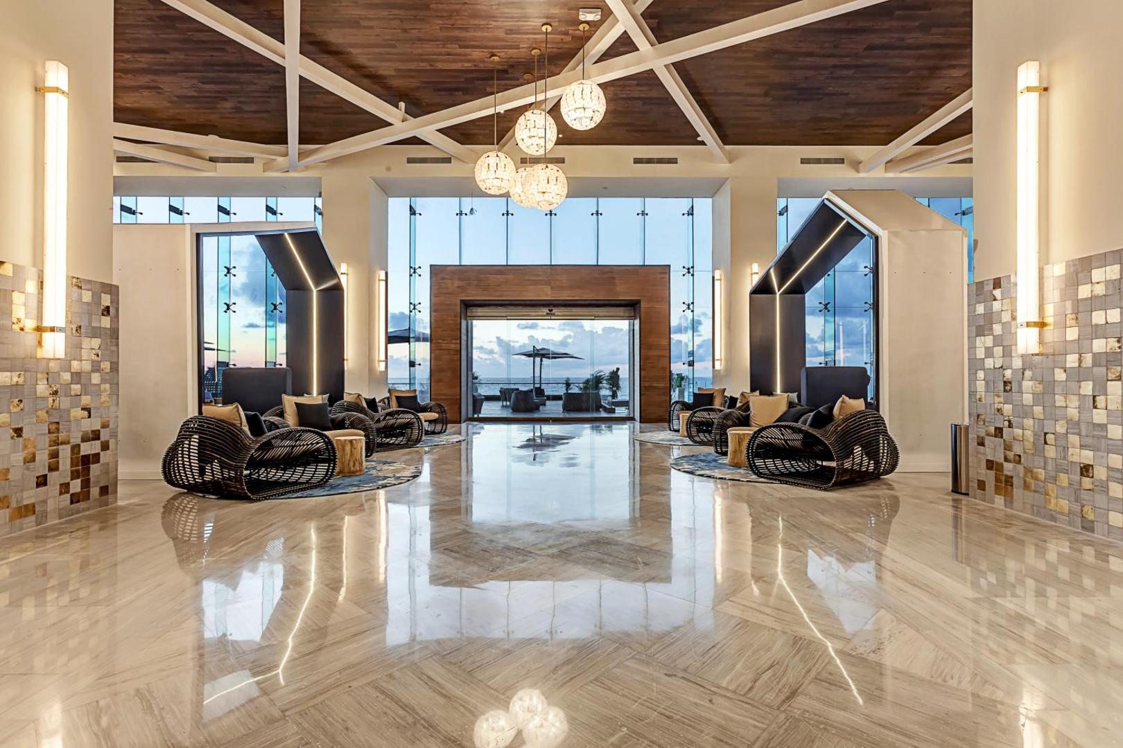 Royalton CHIC Cancun lobby ar modernām mēbelēm, marmora grīdu un skatu uz Karību jūru saulrietā Meksikā