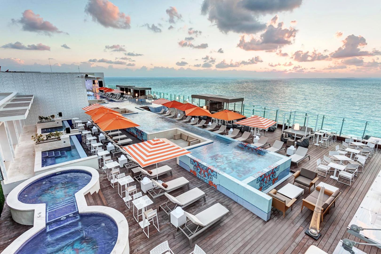 Royalton CHIC Cancun jumta terase ar vairākiem baseiniem, sauļošanās krēsliem un skatu uz Karību jūru saulrietā