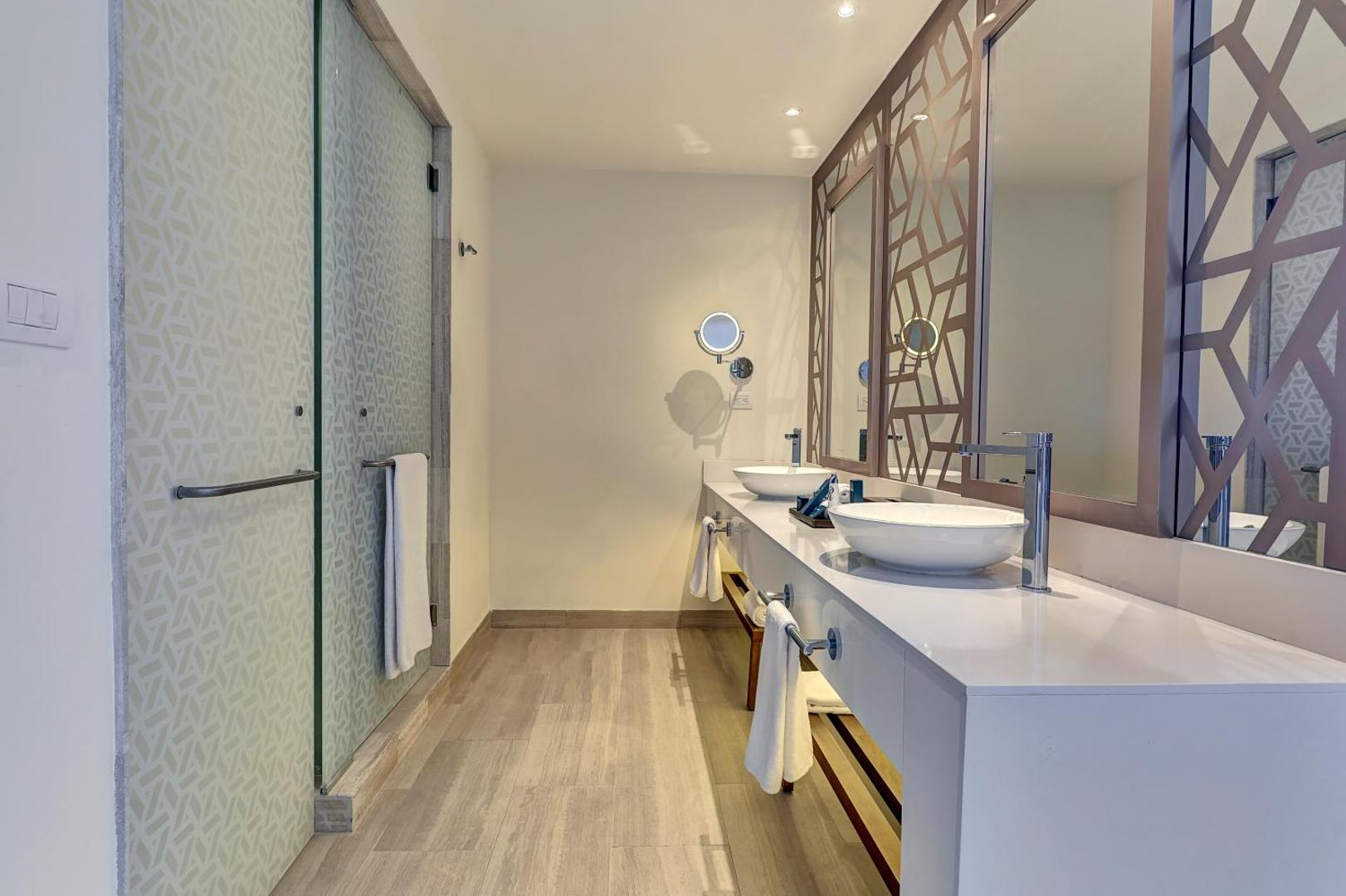 Royalton CHIC Cancun plašā vannas istaba ar dubulto izlietni, lieliem spoguļiem un modernu apdari gaišos toņos.