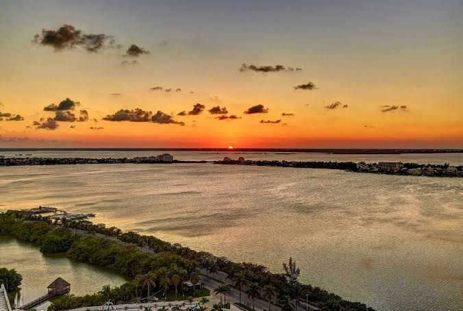 Saulriets virs Kankunas lagūnas no Royalton CHIC Cancun viesnīcas — oranžas debesis un skats uz piekrastes līniju