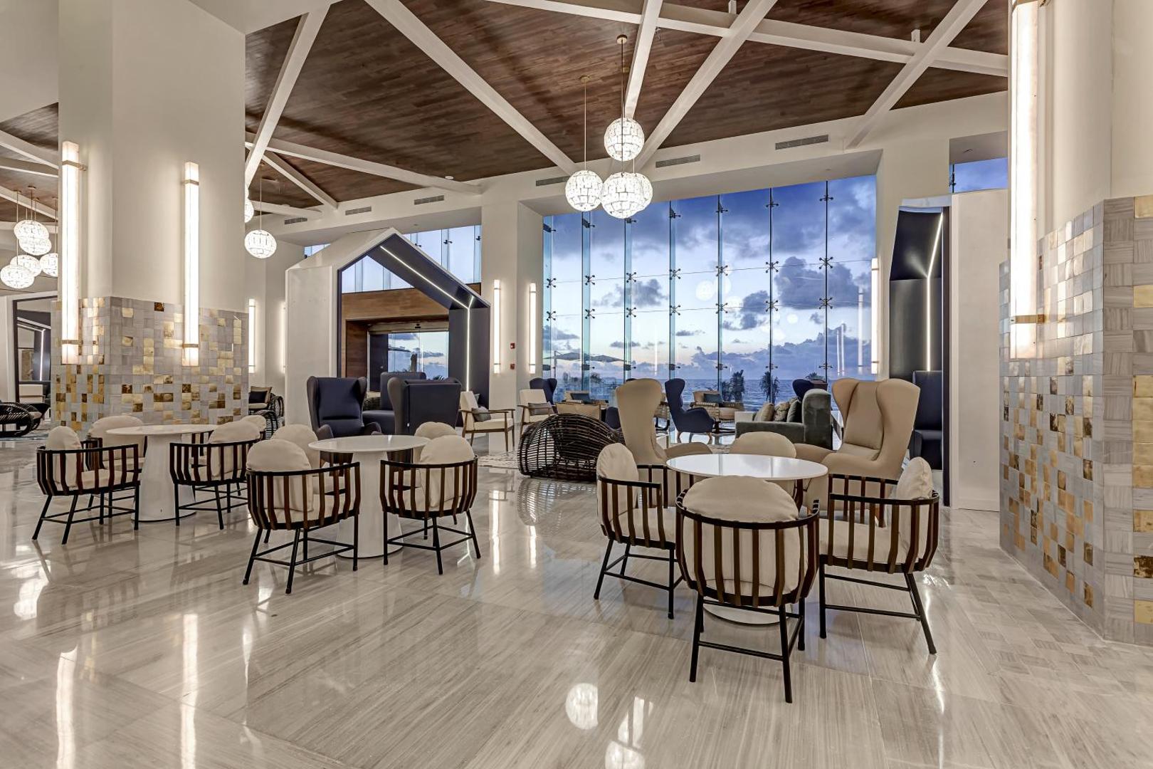 Royalton CHIC Cancun atpūtas zona ar dizaina krēsliem, galdiņiem un lieliem logiem uz okeāna pusi Kankunā