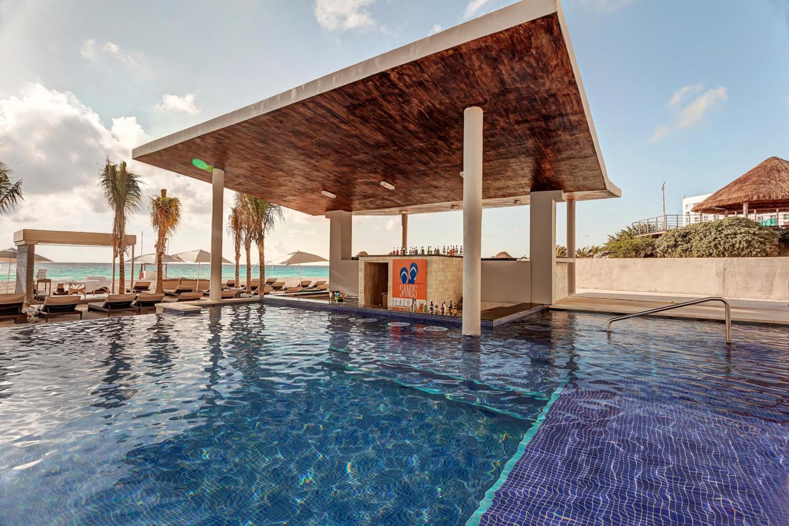 Royalton CHIC Cancun baseina bārs Sands Beach Club ar modernu jumta konstrukciju un bāra krēsliem ūdenī