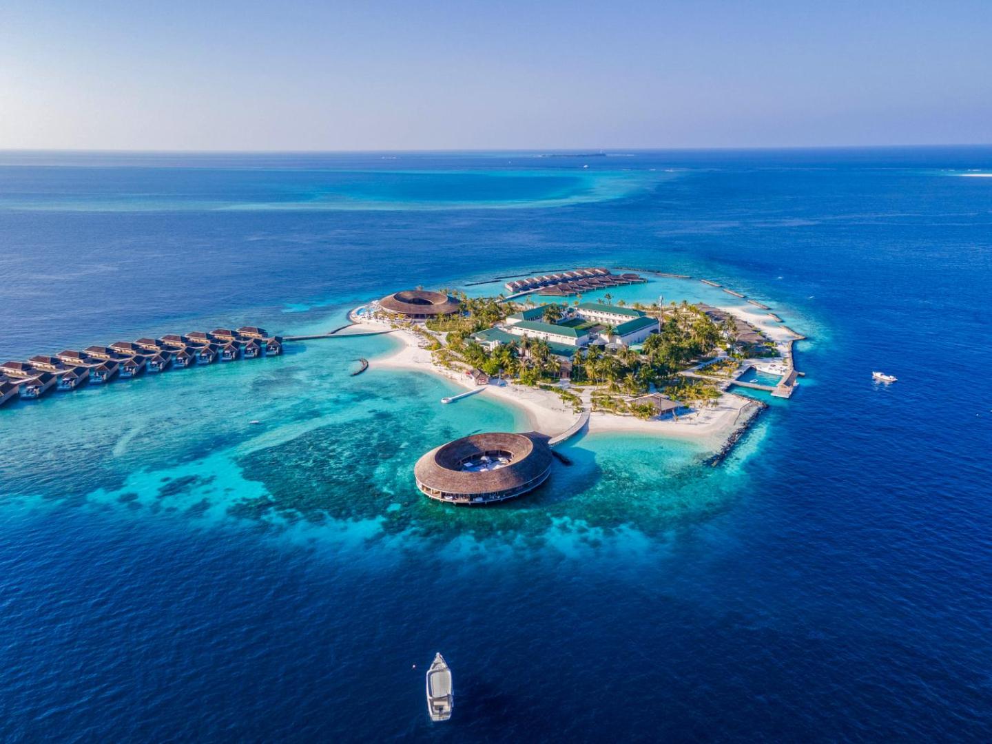 Kagi Maldives Resort & Spa aerofotoattēls no putna lidojuma — privāta sala ar tirkīza lagūnu, ūdens bungalo un apaļu spa c...
