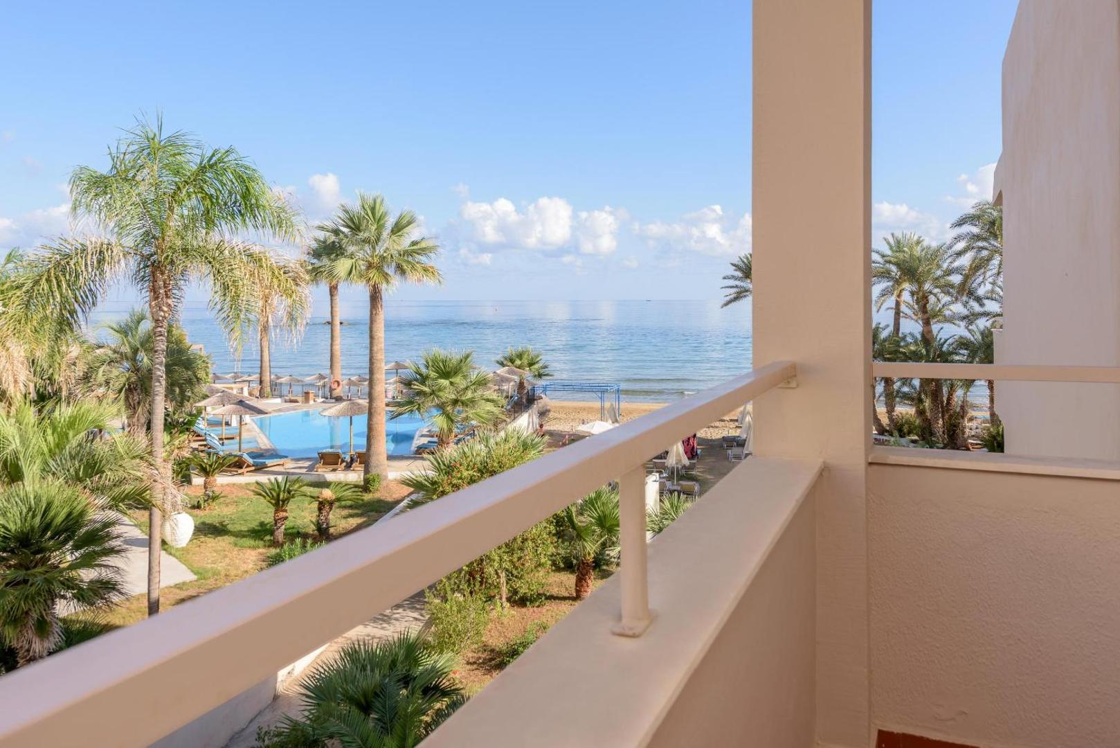 Skats no Zeus Palm Beach Hotel balkona uz āra baseinu, palmām un zilo Vidusjūru Krētas salā