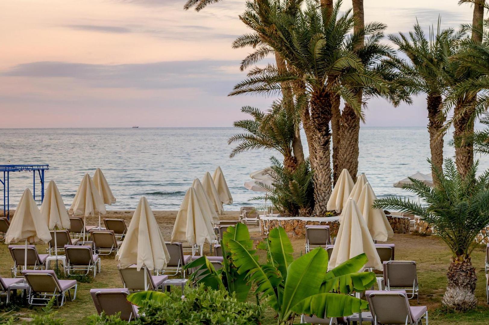 Atpūtas zona ar sauļošanās krēsliem un saulessargiem Zeus Palm Beach Hotel dārzā pie pludmales Krētā