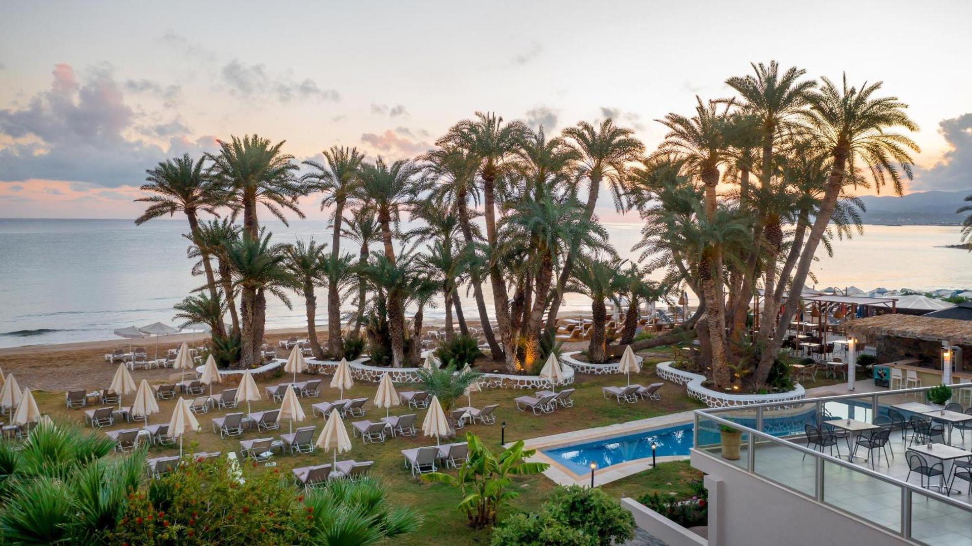 Panorāmas skats no Zeus Palm Beach Hotel terases uz palmu dārzu, baseinu un Vidusjūras piekrasti saullēkta laikā.