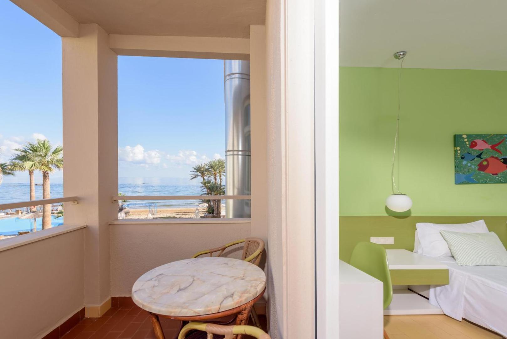 Gaišs Zeus Palm Beach Hotel numurs ar balkonu, kur atrodas galdiņš, un skatu uz jūru un baseinu