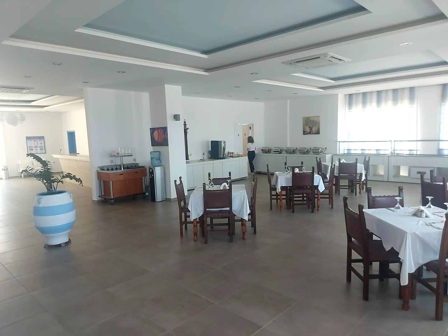 Zeus Palm Beach Hotel restorāna zāle ar klātiem galdiem, koka krēsliem un bufetes zonu gaišā, plašā telpā