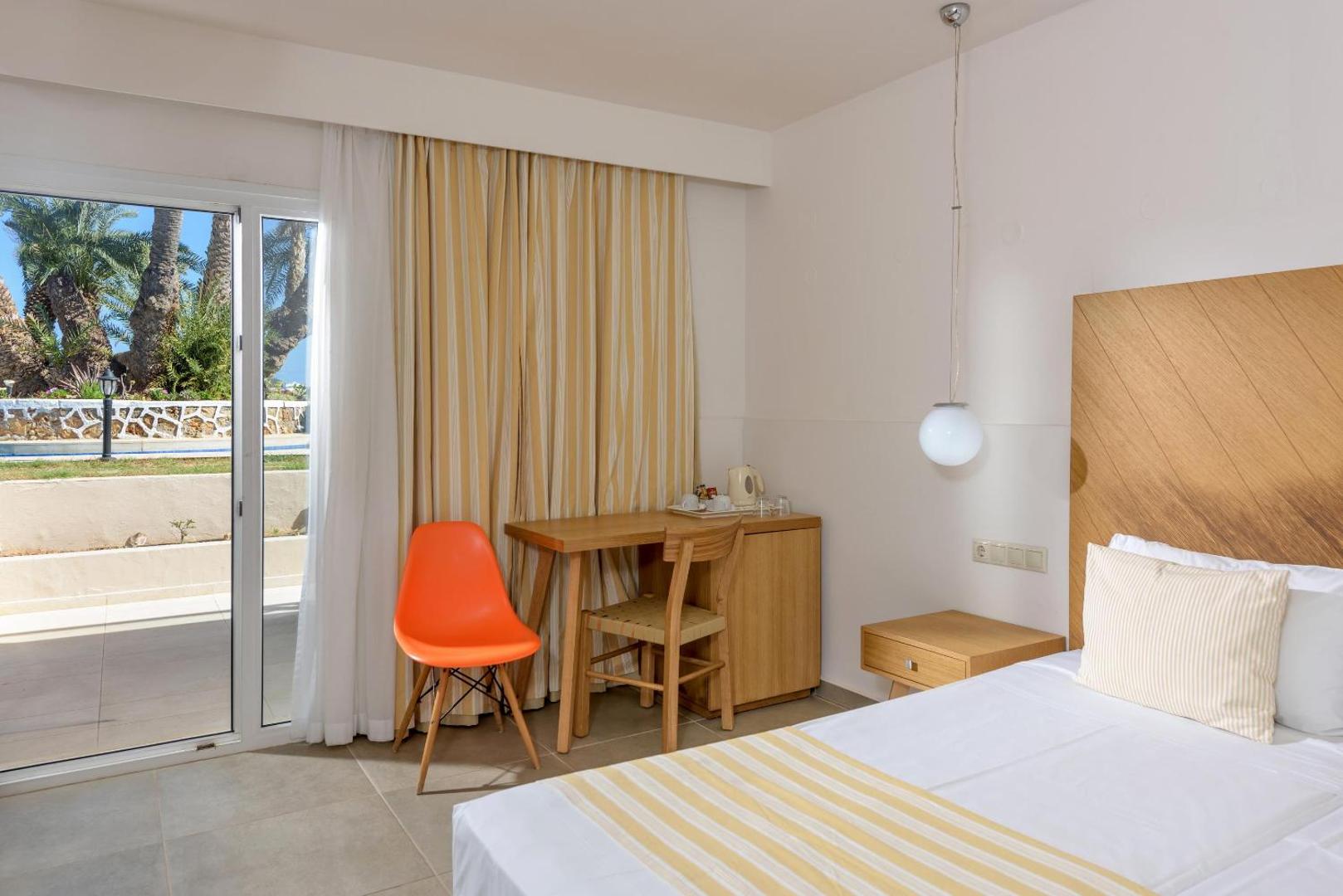 Moderns Zeus Palm Beach Hotel numurs ar gaišām mēbelēm, koka apdari un izeju uz terasi dārza pusē